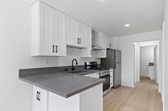 kitchen featuring stainless steel gas range, light wood finished floors, a sink, wall chimney range hood, and dark countertops