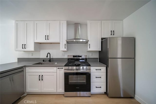 kitchen with stainless steel appliances, light wood-style floors, wall chimney range hood, white cabinets, and a sink