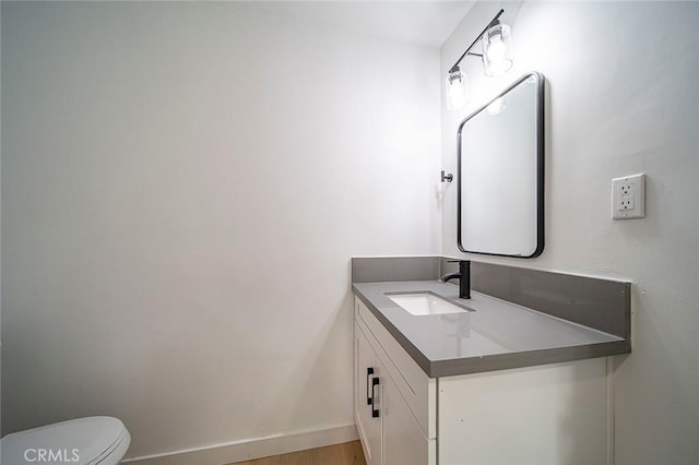 half bathroom with toilet, wood finished floors, vanity, and baseboards