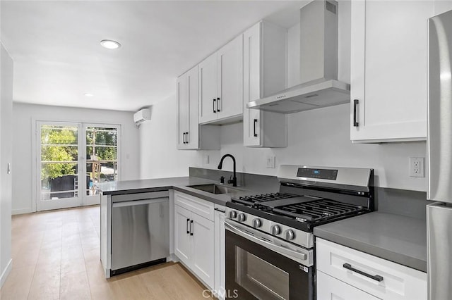 kitchen featuring appliances with stainless steel finishes, wall chimney range hood, white cabinets, dark countertops, and a sink