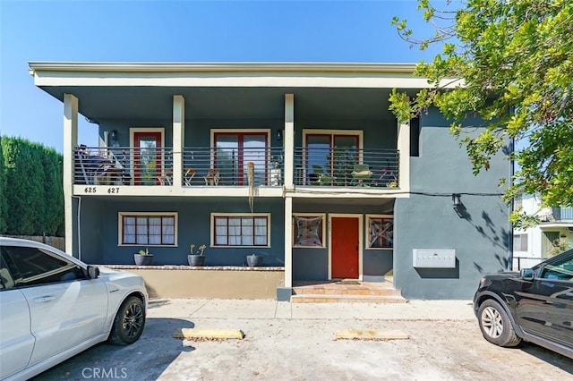 view of front of home featuring a balcony, uncovered parking, and stucco siding