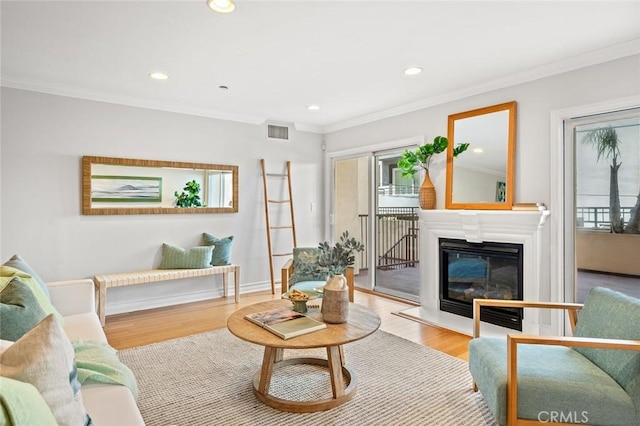 living room featuring recessed lighting, a glass covered fireplace, crown molding, visible vents, and wood finished floors