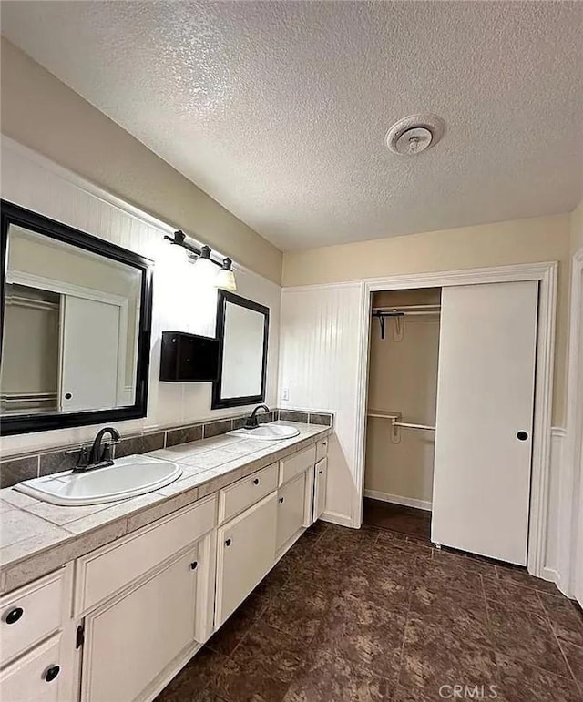 full bath featuring double vanity, a textured ceiling, a spacious closet, and a sink