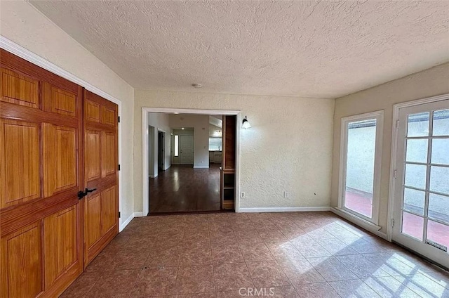 unfurnished room featuring baseboards, tile patterned floors, a textured ceiling, and a textured wall