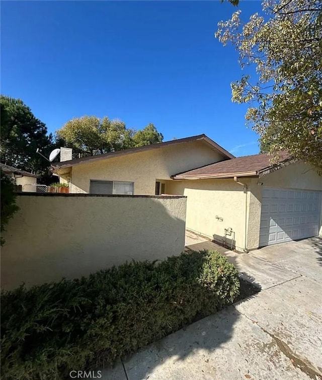 view of property exterior featuring stucco siding, fence, concrete driveway, and an attached garage