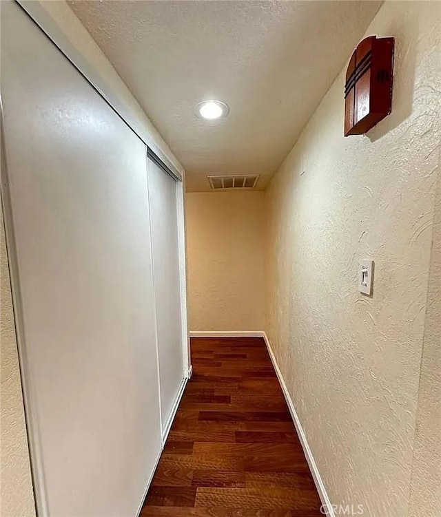 hallway with recessed lighting, wood finished floors, a textured wall, baseboards, and visible vents