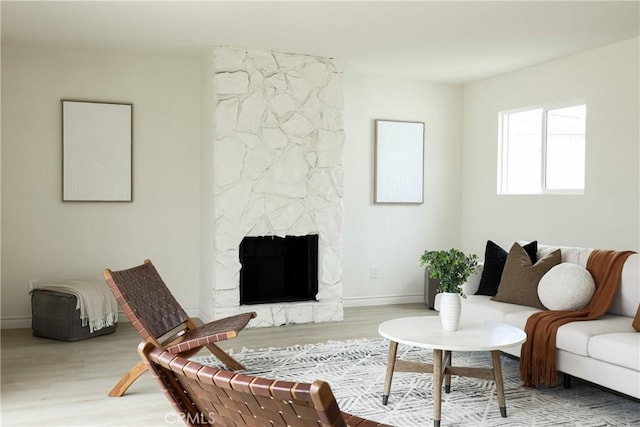 living area featuring a stone fireplace, wood finished floors, and baseboards