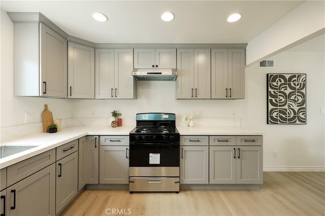 kitchen with under cabinet range hood, gray cabinets, light wood-style flooring, stainless steel gas stove, and light countertops