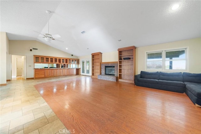 living area with built in shelves, a brick fireplace, visible vents, a ceiling fan, and high vaulted ceiling