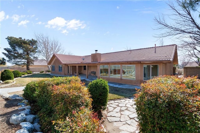 back of house featuring a chimney, a tiled roof, a patio area, stucco siding, and fence