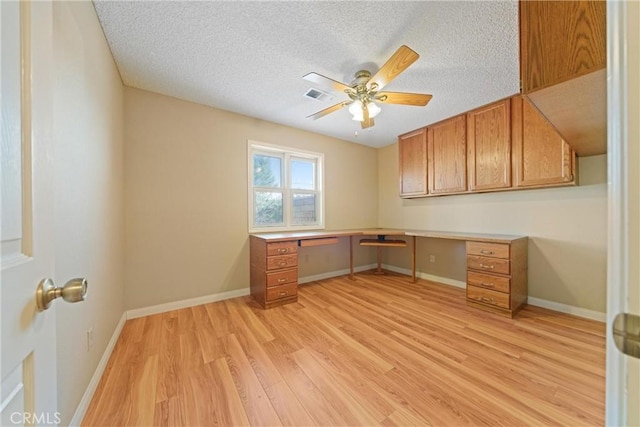 unfurnished office with light wood-type flooring, built in study area, visible vents, a ceiling fan, and a textured ceiling