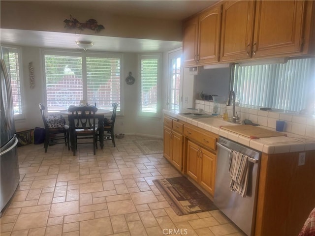 kitchen featuring tasteful backsplash, a sink, appliances with stainless steel finishes, tile counters, and baseboards