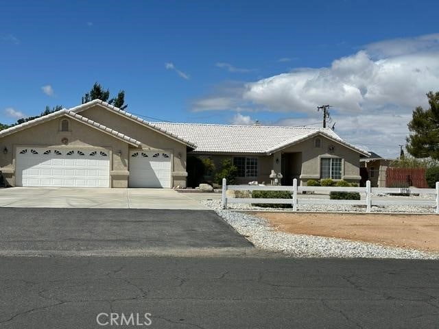 ranch-style home with driveway, a tile roof, an attached garage, stucco siding, and a fenced front yard