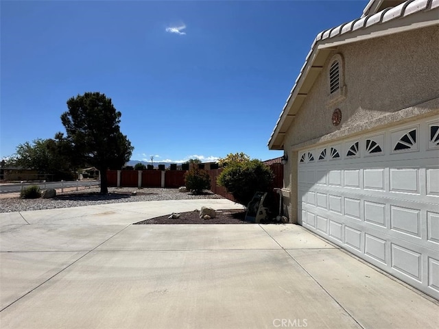 view of home's exterior with concrete driveway, stucco siding, and fence