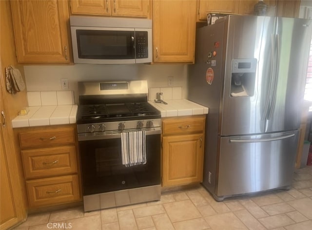 kitchen featuring tile counters, stone finish floor, and appliances with stainless steel finishes
