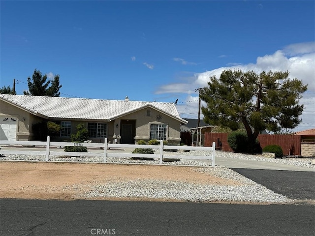 ranch-style home with a tile roof, stucco siding, a fenced front yard, and driveway