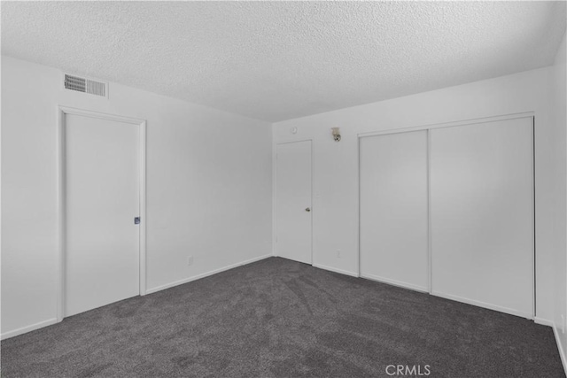unfurnished bedroom with visible vents, dark colored carpet, a textured ceiling, and a closet