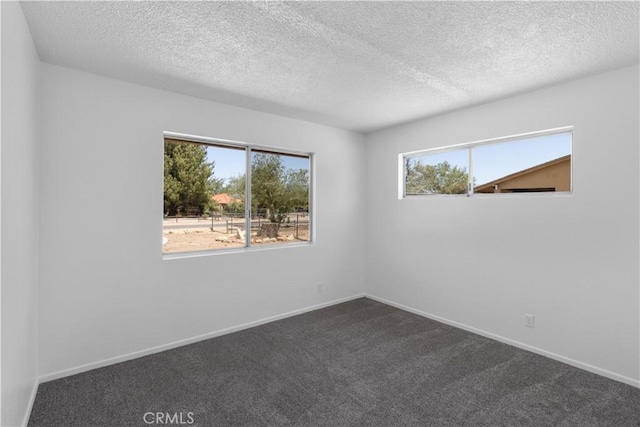 empty room featuring dark carpet, a wealth of natural light, and a textured ceiling