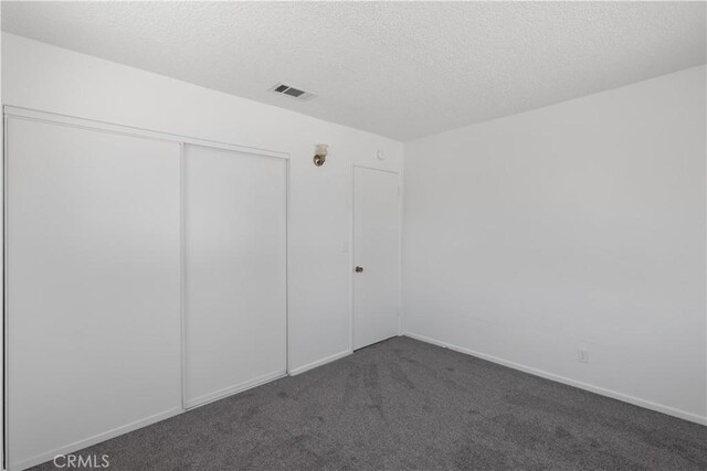 unfurnished bedroom featuring a closet, dark colored carpet, baseboards, visible vents, and a textured ceiling