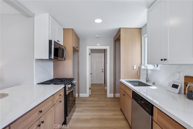 kitchen with a sink, baseboards, light countertops, light wood finished floors, and stainless steel appliances