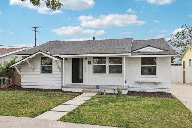 view of front of house featuring roof with shingles, fence, and a front yard