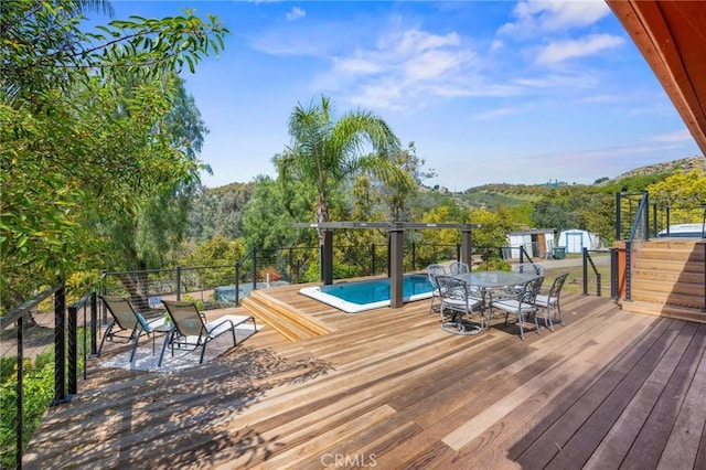 wooden deck with outdoor dining space, an outbuilding, a fenced in pool, and a storage shed
