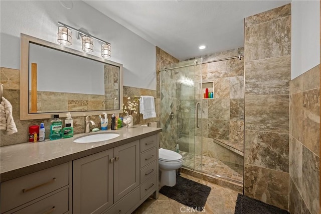 bathroom featuring vanity, toilet, a stall shower, and tile walls