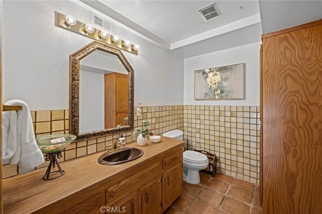 bathroom featuring tile walls, vanity, toilet, a wainscoted wall, and visible vents