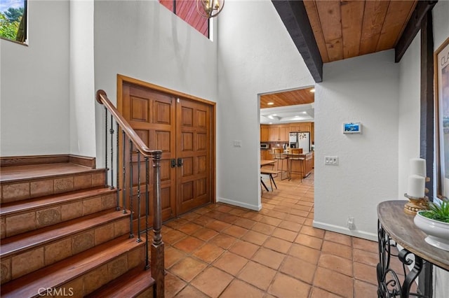 entrance foyer with a high ceiling, wooden ceiling, stairway, baseboards, and tile patterned flooring