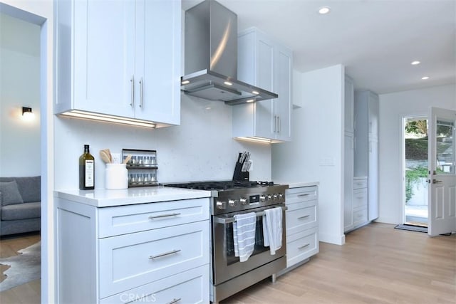 kitchen featuring wall chimney range hood, light wood-style floors, light countertops, stainless steel gas stove, and recessed lighting