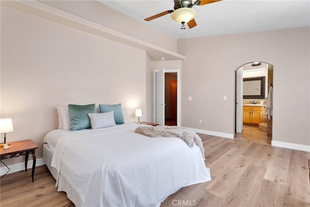 bedroom with a ceiling fan, light wood-style flooring, baseboards, arched walkways, and ensuite bathroom