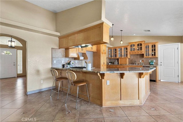 kitchen featuring dark stone countertops, visible vents, tasteful backsplash, and a breakfast bar area