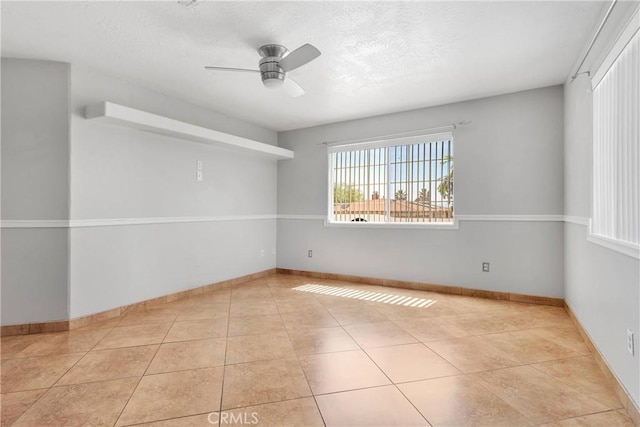 tiled spare room featuring baseboards, a ceiling fan, and a textured ceiling