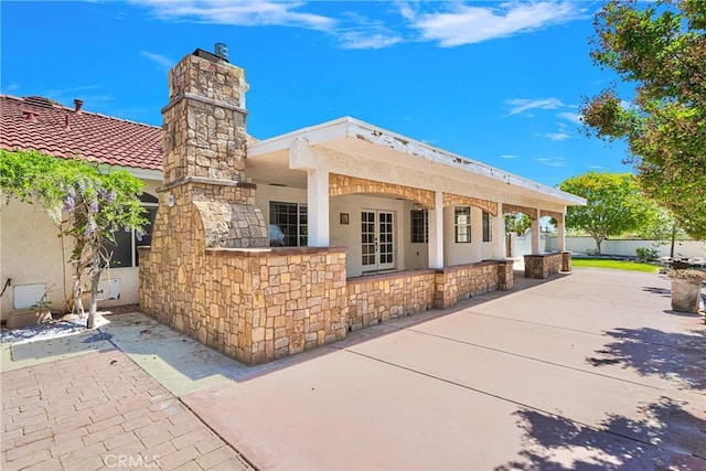 rear view of property with a chimney, fence, stucco siding, and stone siding