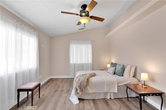 bedroom with lofted ceiling, light wood-type flooring, baseboards, and multiple windows