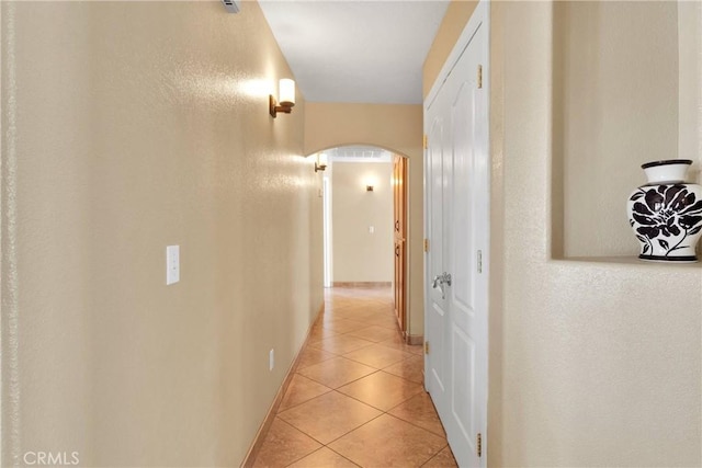 hallway with light tile patterned floors, baseboards, and arched walkways