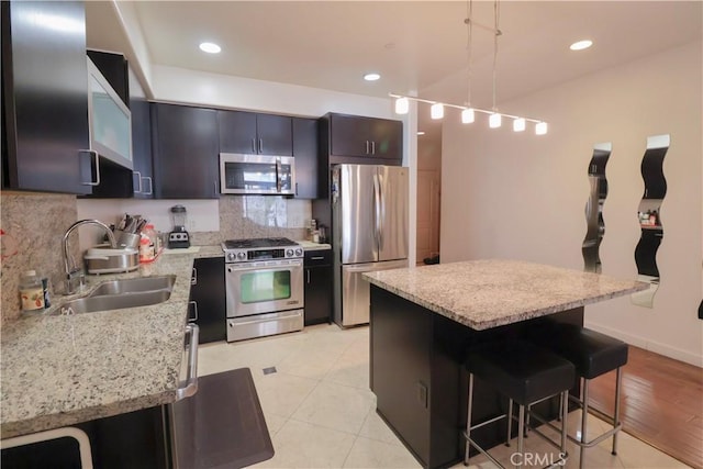 kitchen with a breakfast bar, appliances with stainless steel finishes, backsplash, a sink, and pendant lighting