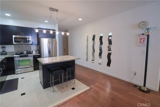 kitchen with a breakfast bar area, tasteful backsplash, appliances with stainless steel finishes, a kitchen island, and decorative light fixtures