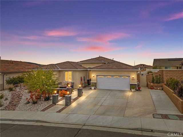 ranch-style home featuring stucco siding, a tiled roof, concrete driveway, an attached garage, and fence