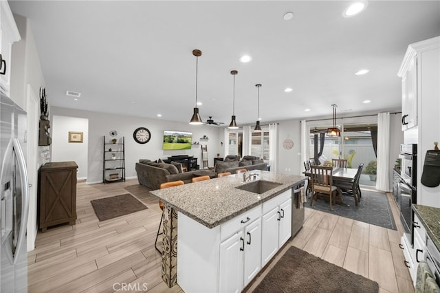 kitchen featuring a sink, stainless steel appliances, light stone countertops, wood finish floors, and a kitchen island with sink