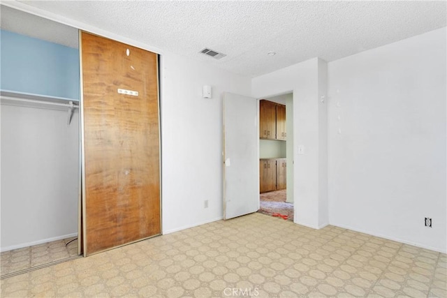 unfurnished bedroom featuring a textured ceiling, visible vents, a closet, baseboards, and tile patterned floors