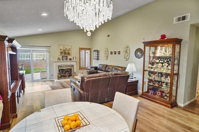dining area with an inviting chandelier, a fireplace with raised hearth, visible vents, vaulted ceiling, and wood finished floors