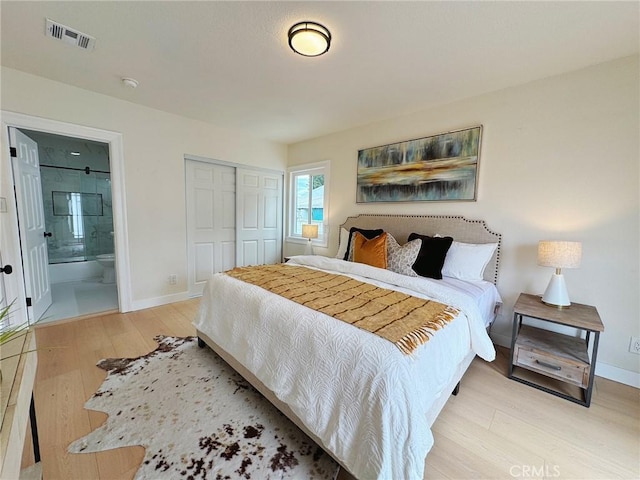 bedroom with visible vents, a closet, wood finished floors, baseboards, and ensuite bath