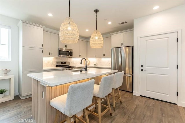 kitchen with decorative backsplash, a sink, appliances with stainless steel finishes, light countertops, and a center island with sink