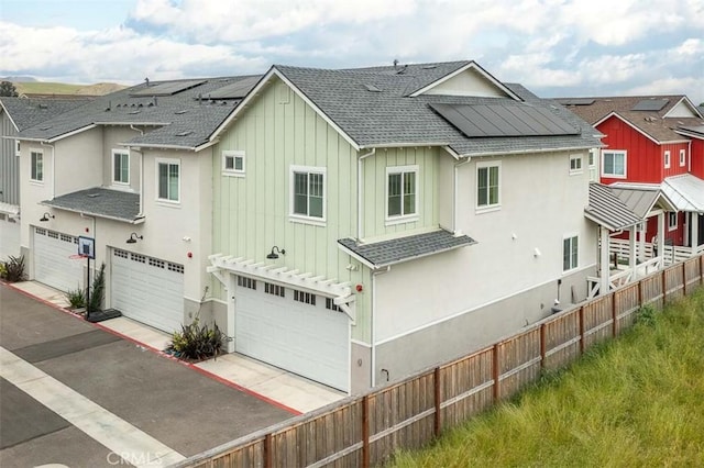 back of property with board and batten siding, roof mounted solar panels, an attached garage, and roof with shingles