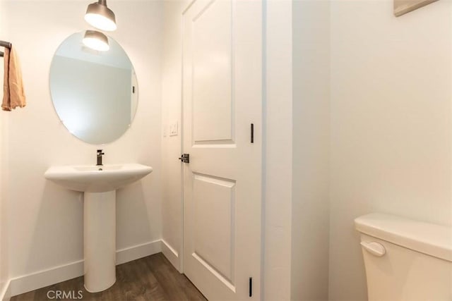 half bath featuring wood finished floors, toilet, and baseboards
