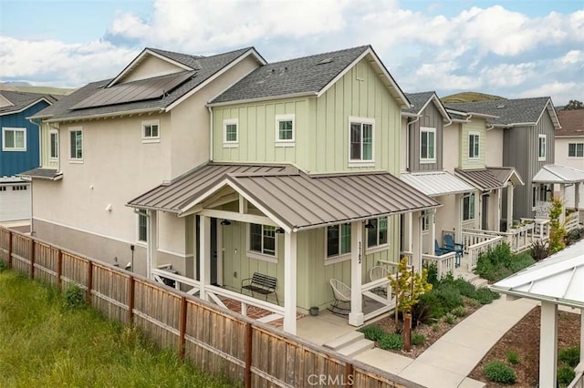rear view of property featuring board and batten siding, a standing seam roof, fence, a shingled roof, and a residential view