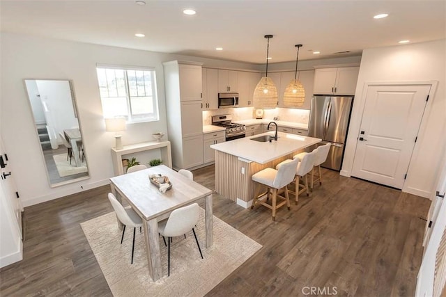 kitchen with a sink, backsplash, light countertops, appliances with stainless steel finishes, and an island with sink