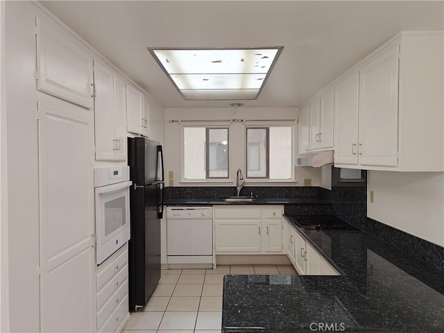 kitchen featuring white cabinetry, a sink, dark stone countertops, light tile patterned floors, and black appliances