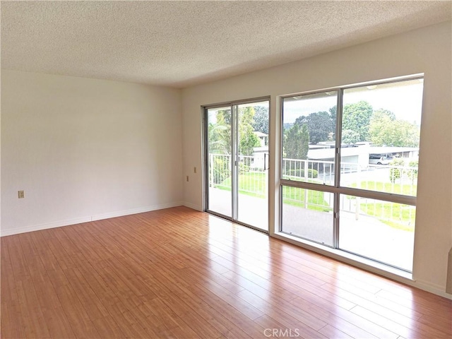 empty room with baseboards, a textured ceiling, and wood finished floors